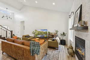 Living room with a large fireplace, light wood-style flooring, stairway, high vaulted ceiling, and recessed lighting