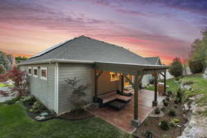 Rear view of property featuring roof with shingles, a patio, a yard, and solar panels