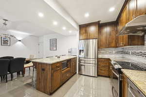 Kitchen featuring stainless steel appliances, a peninsula, recessed lighting, light stone countertops, and decorative backsplash