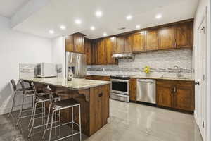 Kitchen featuring decorative backsplash, appliances with stainless steel finishes, light stone counters, a peninsula, and recessed lighting
