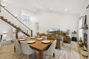 Dining room with stairs, a large fireplace, light wood-type flooring, and high vaulted ceiling