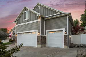 View of front facade featuring board and batten siding, driveway, an attached garage, and brick siding