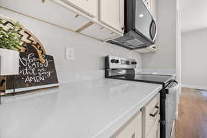 Kitchen with stainless steel appliances, white cabinetry, light wood-style flooring, and light stone counters