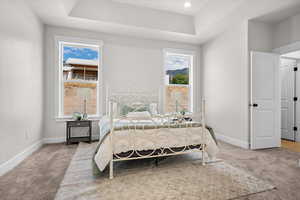 Bedroom with light colored carpet, a raised ceiling, and recessed lighting