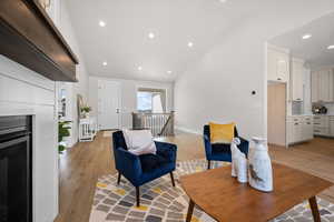 Living area with an upstairs landing, light wood-style flooring, recessed lighting, a fireplace, and high vaulted ceiling