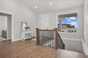 Corridor with an upstairs landing, vaulted ceiling, wood finished floors, and recessed lighting