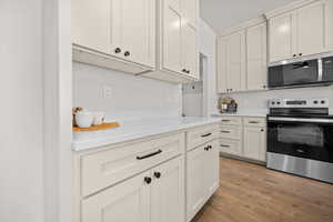 Kitchen featuring appliances with stainless steel finishes, light wood finished floors, and white cabinets