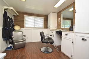 Home office with dark wood-style flooring, a decorative wall, wooden walls, and a wainscoted wall