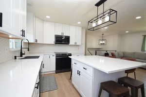 Kitchen with a breakfast bar, light wood finished floors, range with electric stovetop, stainless steel microwave, and white cabinets
