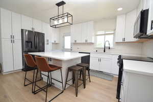 Kitchen featuring stainless steel appliances, a breakfast bar area, a center island, light wood finished floors, and white cabinets