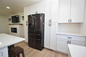 Kitchen featuring stainless steel fridge, light wood-style floors, white cabinetry, a glass covered fireplace, and recessed lighting