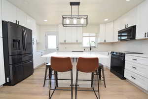 Kitchen featuring stainless steel fridge, black / electric stove, a breakfast bar area, a kitchen island, and white cabinetry
