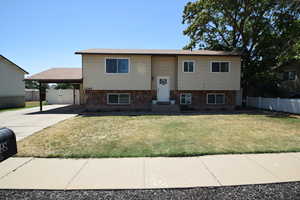 Bi-level home with an attached carport, concrete driveway, stone siding, and a gate