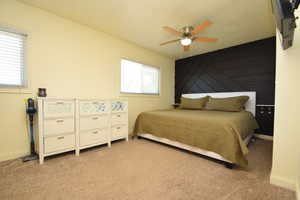 Bedroom featuring light colored carpet, ornamental molding, wooden walls, and a ceiling fan
