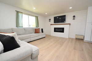 Living area with light wood-style flooring, a glass covered fireplace, wooden walls, and recessed lighting