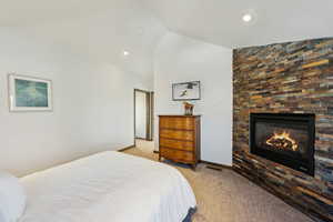 Bedroom with light carpet, vaulted ceiling, a glass covered fireplace, and recessed lighting