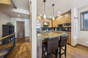 Kitchen with wood-type flooring, decorative backsplash, recessed lighting, a breakfast bar area, and under cabinet range hood