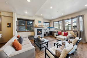 Living room with wood finished floors, a glass covered fireplace, and recessed lighting