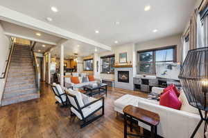 Living area featuring recessed lighting, plenty of natural light, stairway, dark wood-style flooring, and a glass covered fireplace