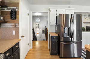 Kitchen with stainless steel fridge, white cabinets, light wood-style floors, light countertops, and dark cabinetry