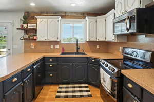 Kitchen with electric range oven, stainless steel microwave, black dishwasher, white cabinetry, and open shelves