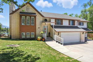 Raised ranch with a chimney, a garage, concrete driveway, roof with shingles, and brick siding