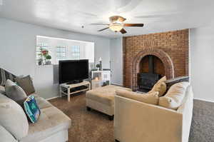 Living area featuring a wood stove, carpet flooring, a ceiling fan, and a textured ceiling