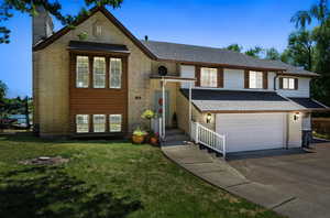 Raised ranch featuring a chimney, a garage, concrete driveway, a front yard, and roof with shingles