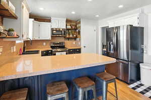 Kitchen with open shelves, appliances with stainless steel finishes, a peninsula, light countertops, and recessed lighting