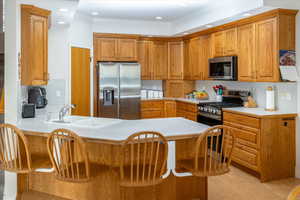 Kitchen with stainless steel appliances, a peninsula, light countertops, ornamental molding, and a breakfast bar area