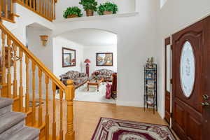 Foyer with light wood-type flooring, arched walkways, crown molding, stairs, and a towering ceiling