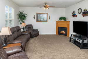 Carpeted living room with crown molding, ceiling fan, and a glass covered fireplace