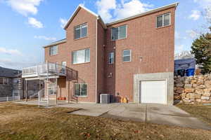 Back of property with brick siding, an attached garage, stairway, a yard, and a patio