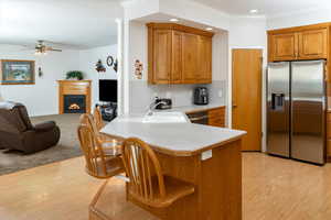 Kitchen with stainless steel appliances, brown cabinetry, a ceiling fan, open floor plan, and ornamental molding