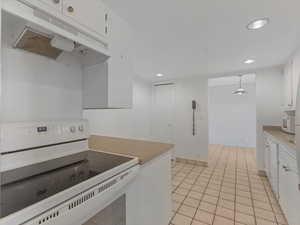 Kitchen with white appliances, under cabinet range hood, white cabinetry, recessed lighting, and light tile patterned floors
