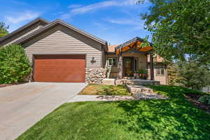 View of front of house featuring an attached garage, stone siding, driveway, and a front lawn