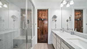 Full bath featuring double vanity, a stall shower, and a chandelier