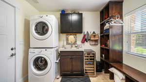 Laundry area with stacked washer / dryer, light stone finish flooring, cabinet space, and wine cooler