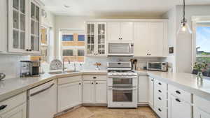 Kitchen featuring white appliances, white cabinetry, and decorative light fixtures