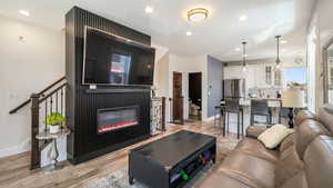 Living room with light wood-type flooring, recessed lighting, and a glass covered fireplace