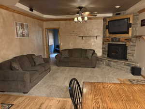 Living area featuring a ceiling fan, a raised ceiling, wood finished floors, and a stone fireplace