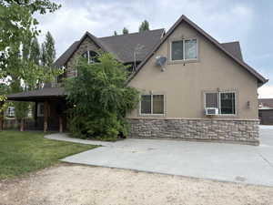 Back of house with stone siding, stucco siding, a shingled roof, and a patio area