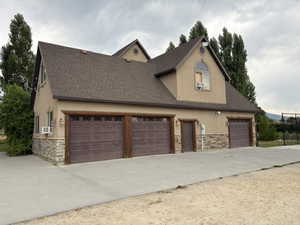 View of front of house with stone siding, a shingled roof, concrete driveway, and stucco siding