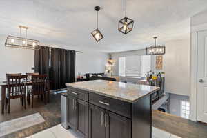 Kitchen featuring a chandelier, a textured ceiling, pendant lighting, light stone counters, and a kitchen island