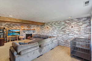 Carpeted living area with a textured ceiling, brick wall, recessed lighting, beamed ceiling, and a warm lit fireplace