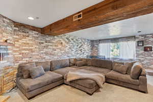 Carpeted living area with brick wall, recessed lighting, and beamed ceiling