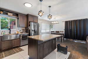 Kitchen featuring stainless steel appliances, dark brown cabinetry, light stone counters, hanging light fixtures, and decorative backsplash