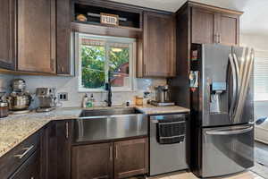 Kitchen with appliances with stainless steel finishes, dark brown cabinets, decorative backsplash, and light stone countertops