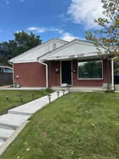 Single story home featuring covered porch, a front lawn, and brick siding