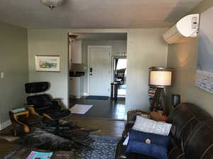 Living room with dark wood-style flooring and a wall unit AC